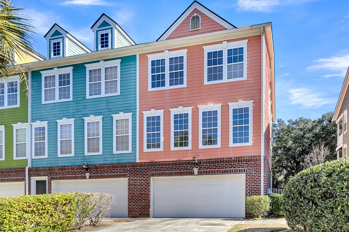 A vibrant exterior shot featuring a colorful facade, large windows, and a brick garage. The setting is inviting, with sunlight casting a warm glow—perfect for outdoor leisure, neighborhood walks, or simply enjoying the view from the patio or upper windows. The overall mood is bright and energetic.