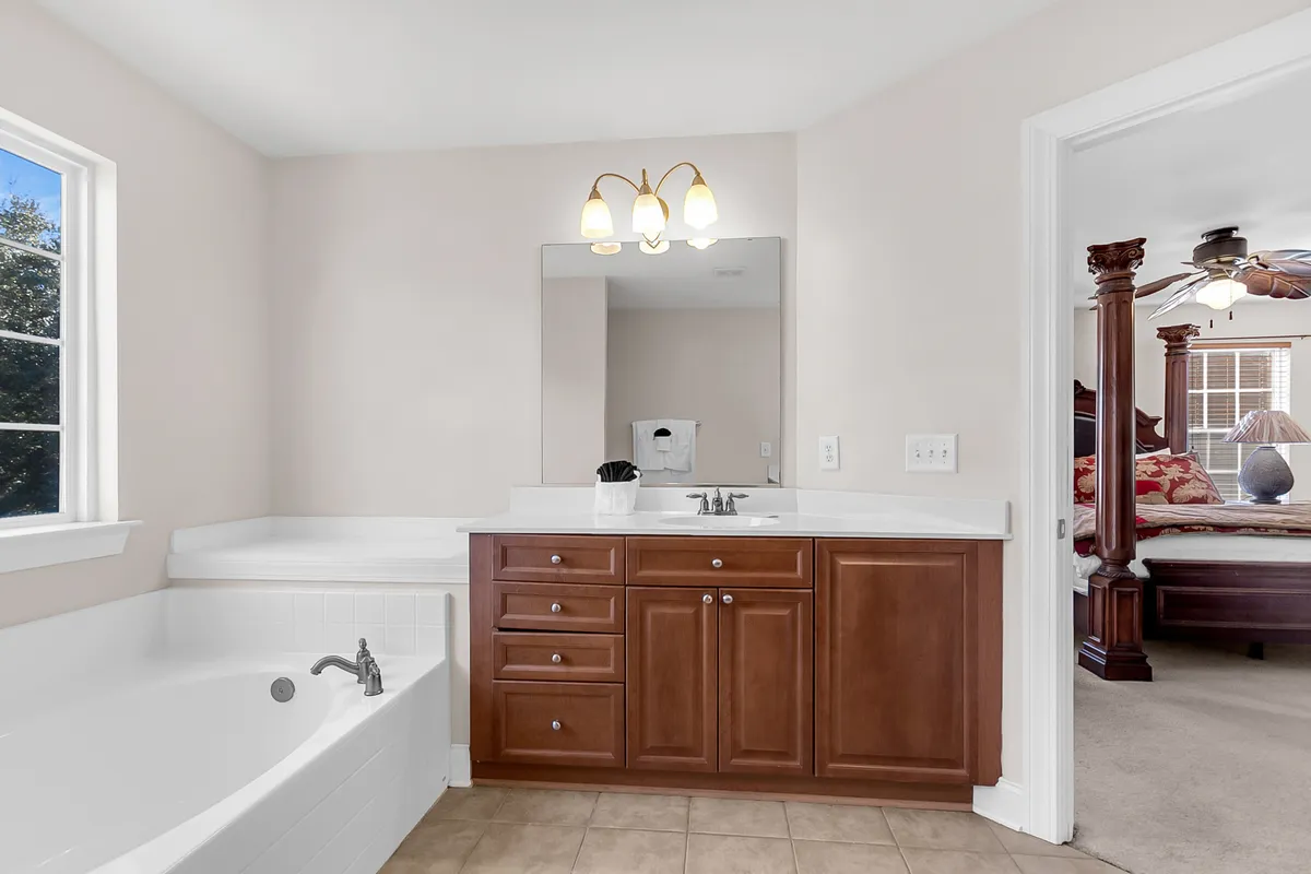 A serene bathroom scene displaying a bathtub, sleek vanity, and a large mirror. The overall feel is luxurious yet peaceful, suggesting a space designed for relaxation and self-care routines.