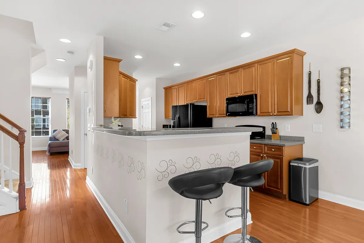 A modern kitchen with an island and bar stools, wooden cabinetry, and stainless steel appliances. The space is bright and inviting, ideal for cooking, entertaining, or casual dining.