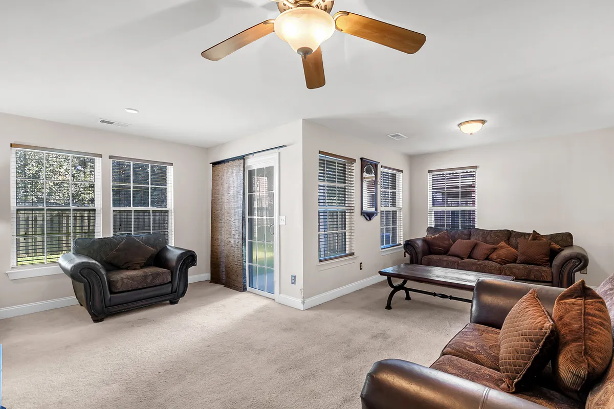 A living room boasting comfortable sofas, large windows that flood the space with daylight, and a ceiling fan for added comfort. The arrangement encourages both group interaction and personal relaxation, set in an environment that feels fresh and open.