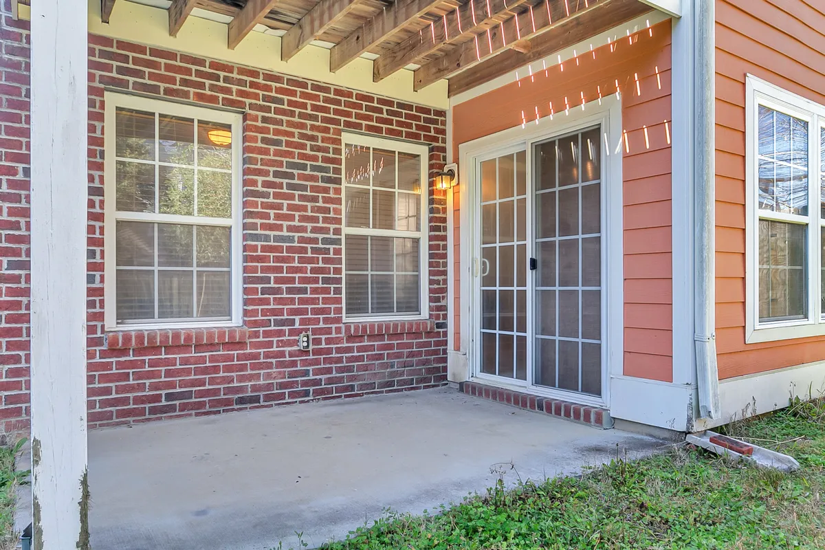 A cozy outdoor patio area framed by a brick wall, glass doors, and wooden beams. The setting is ideal for relaxing with a drink, enjoying the fresh air, or gathering with friends after a day in the city.