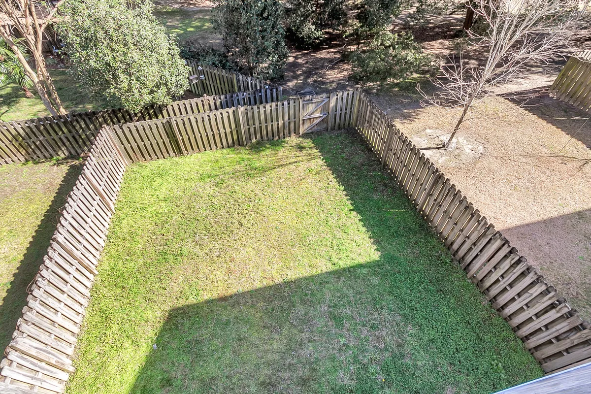 A fenced backyard with green grass, surrounded by mature trees. The space looks tranquil and safe, ideal for children playing, hosting family gatherings, or enjoying quiet moments like morning coffee or watching sunsets. The inviting outdoor area suggests privacy and a direct connection to nature.